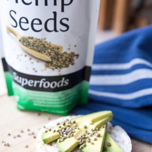 Toasted_Hemp_Seeds_-_Sprinkled_on_rice_cake_with_avocados_on_wood_florr_with_blue_white_cloth_...jpg